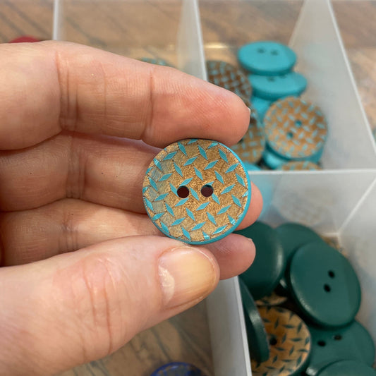 Hand holding a decorative button with a clear container of assorted buttons in the background.