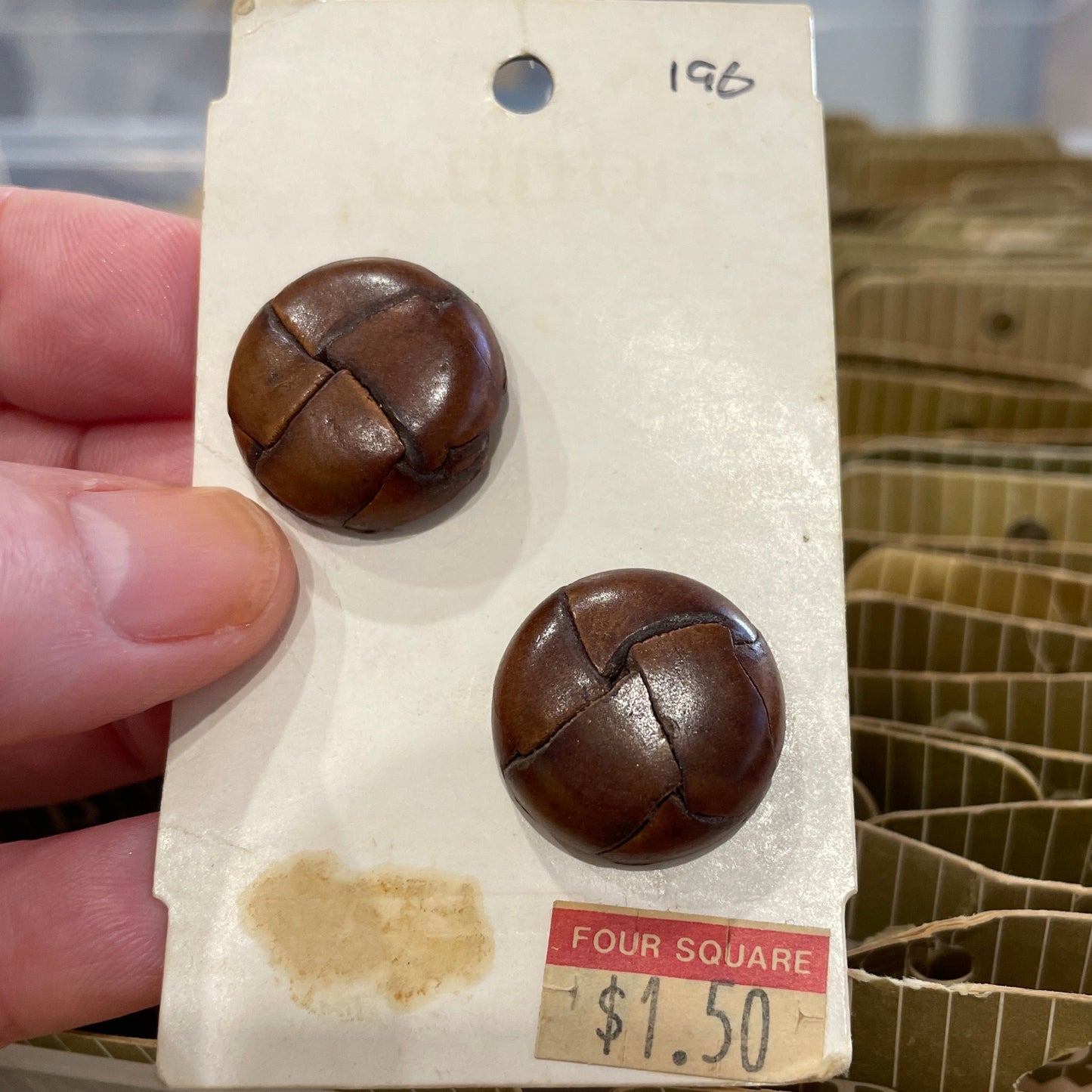 Brown buttons on a card with a price tag held by a hand, blurred background