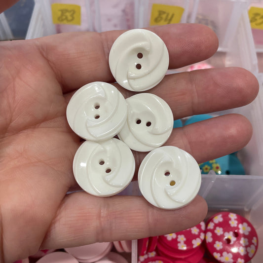 White buttons held in a hand with a container of assorted buttons in the background