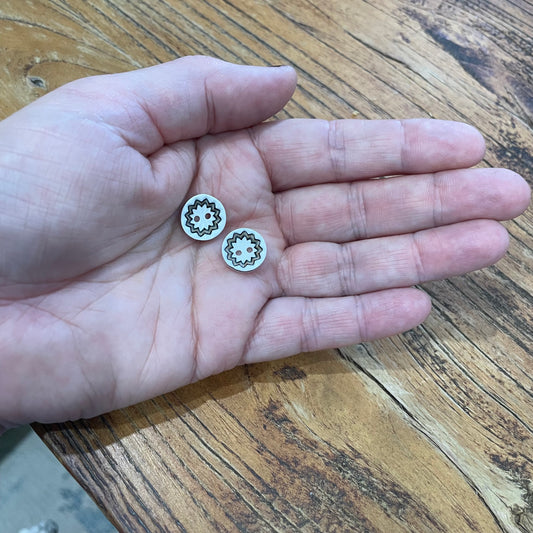 Two small buttons with a gear design held in a hand on a wooden surface.