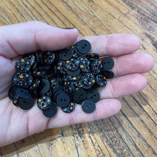 Hand holding a small pile of black buttons with star patterns on a wooden surface
