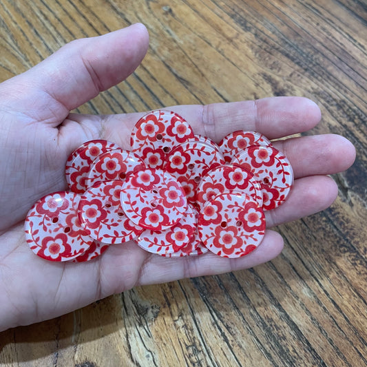 Hand holding red and white floral patterned buttons on a wooden surface