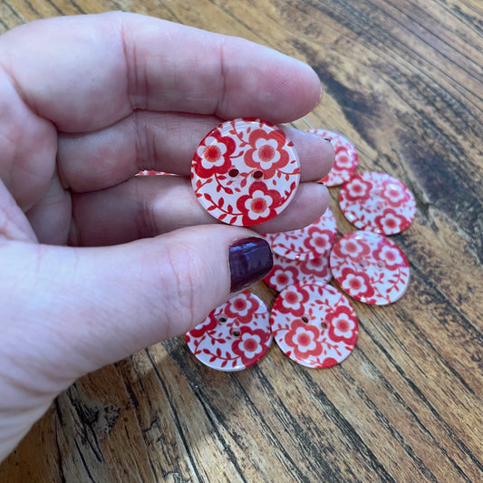 Hand holding red and white floral patterned buttons on a wooden surface