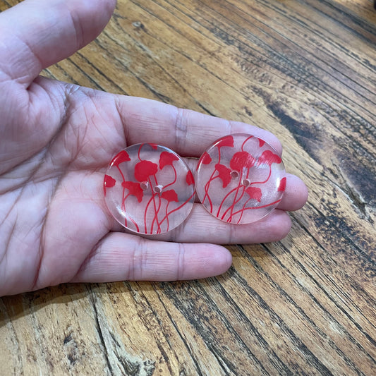 Two red floral buttons held between fingers on a wooden surface