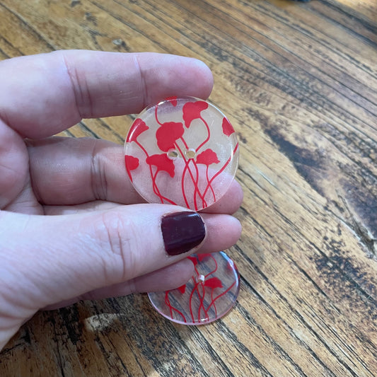 Hand holding a red floral button on a wooden surface