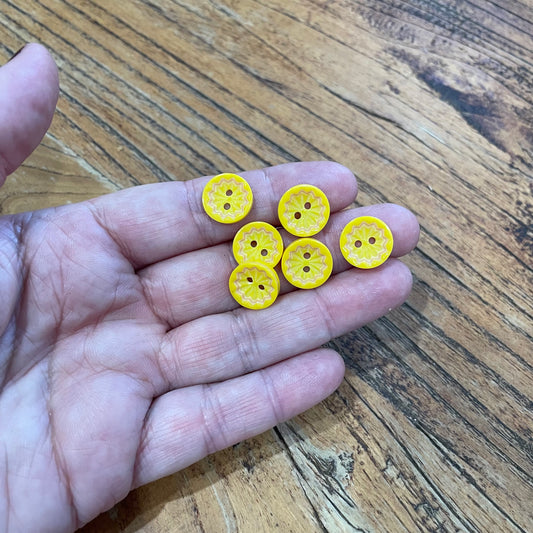 Hand holding six yellow buttons on a wooden surface