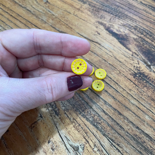 Hand holding small yellow buttons on a wooden surface
