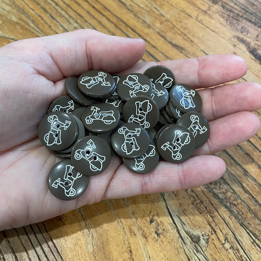 Hand holding a collection of brown buttons with white illustrations on a wooden surface
