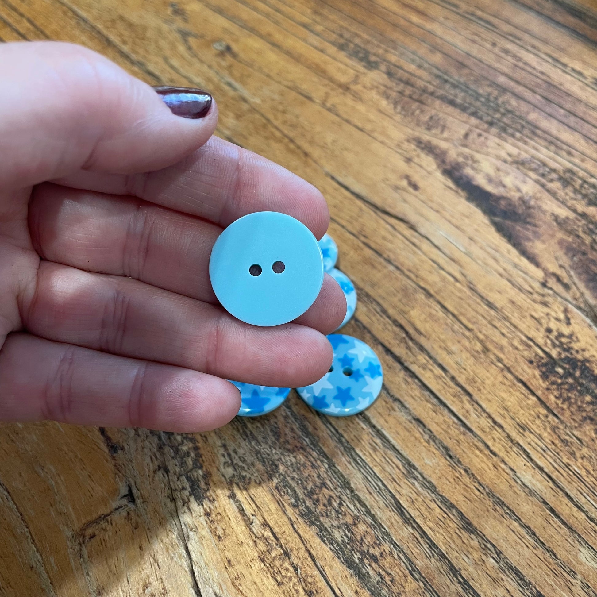 Hand holding a light blue button with more buttons on a wooden surface