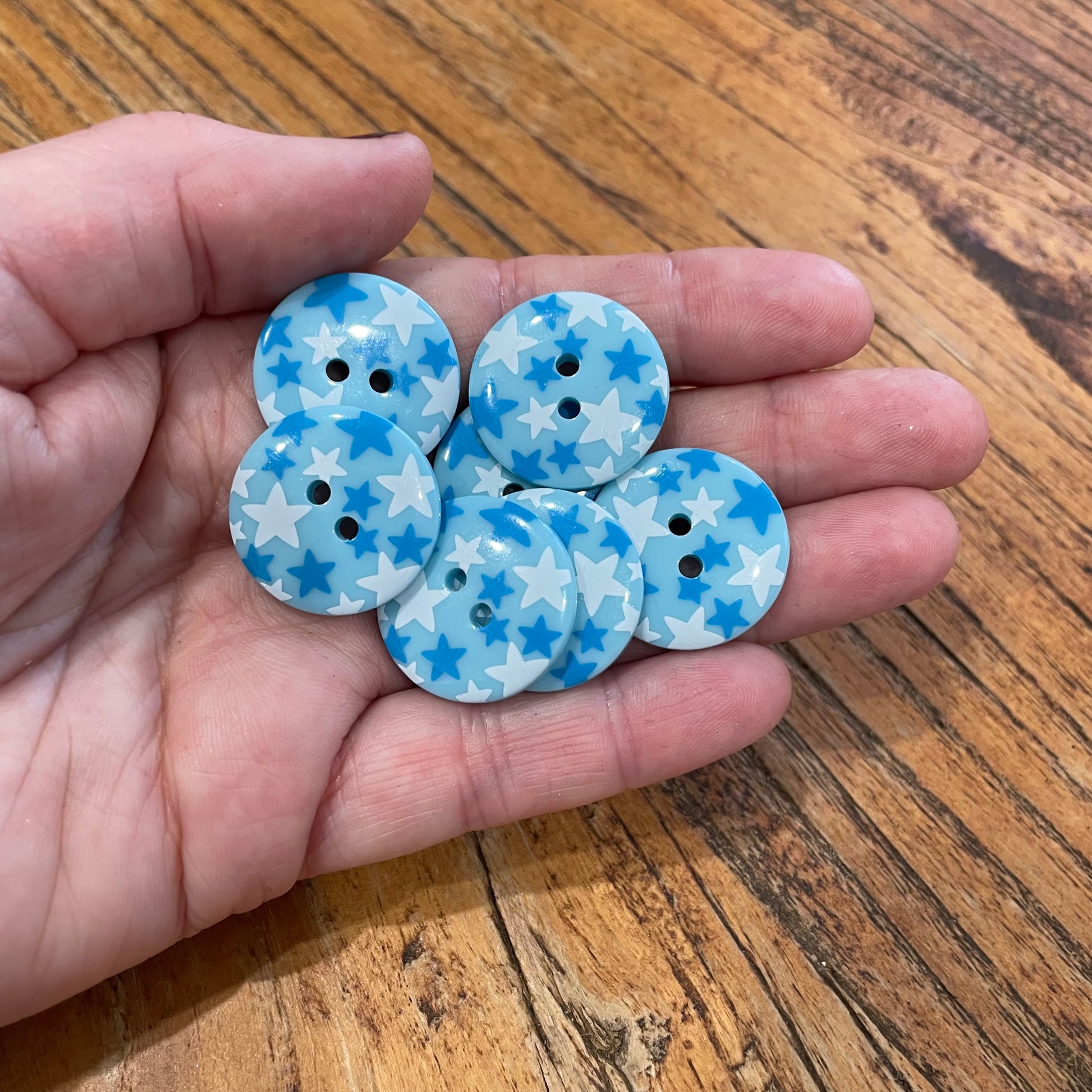 Hand holding blue buttons with star pattern on a wooden surface