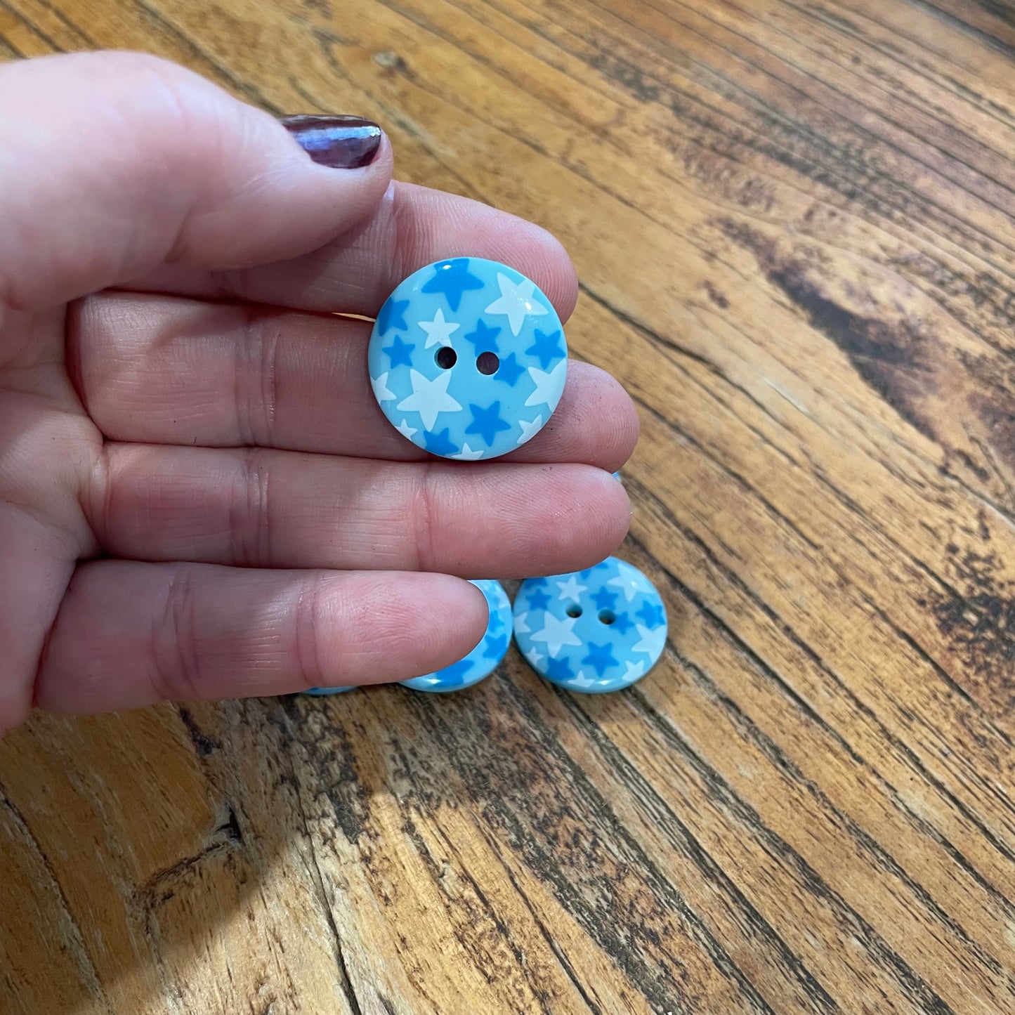 Hand holding two blue and white buttons with star pattern on a wooden surface