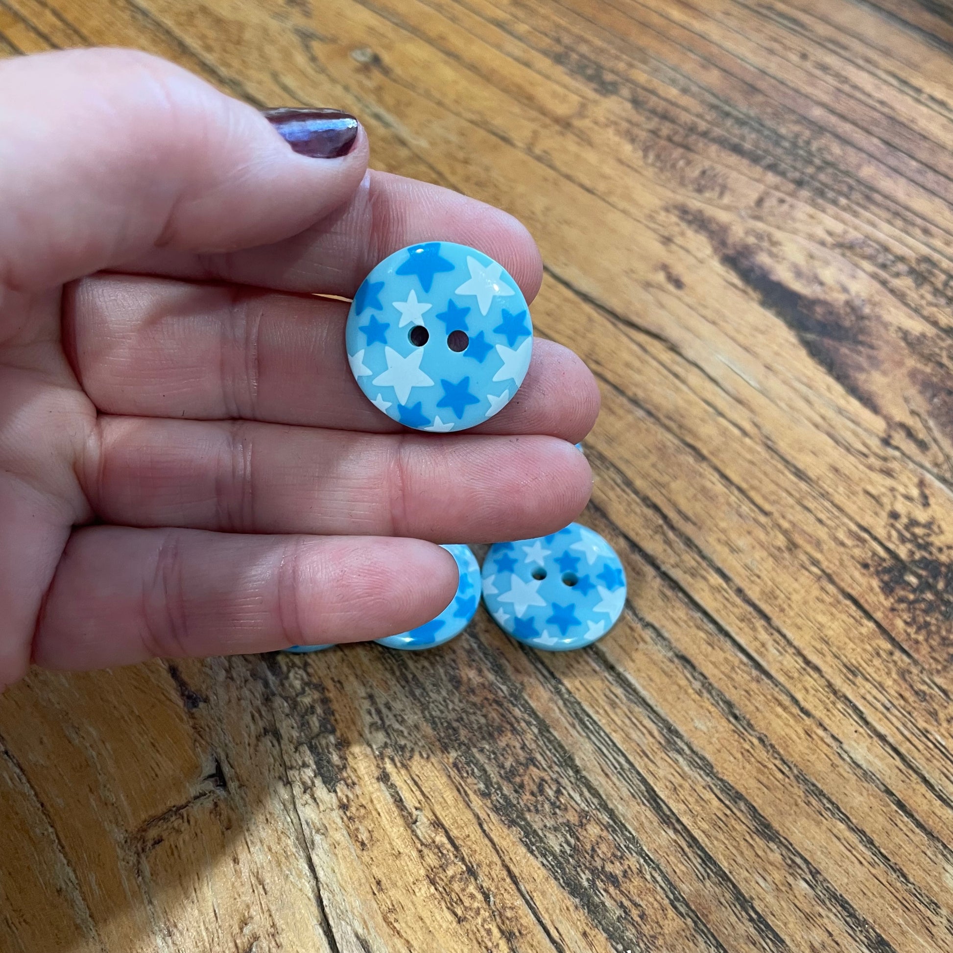 Hand holding two blue and white buttons with star pattern on a wooden surface