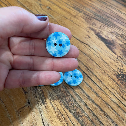 Hand holding two blue and white buttons with star pattern on a wooden surface