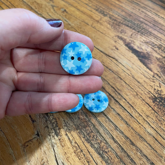 Hand holding two blue and white buttons with star pattern on a wooden surface