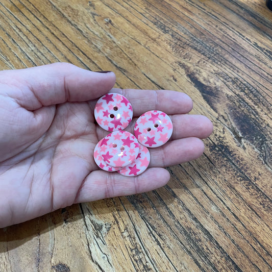 Pink buttons with star pattern held in a hand on a wooden surface