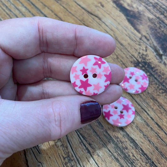 Pink buttons with star pattern held between fingers on a wooden surface