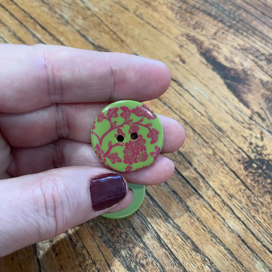 Hand holding a green button with pink floral pattern on a wooden surface