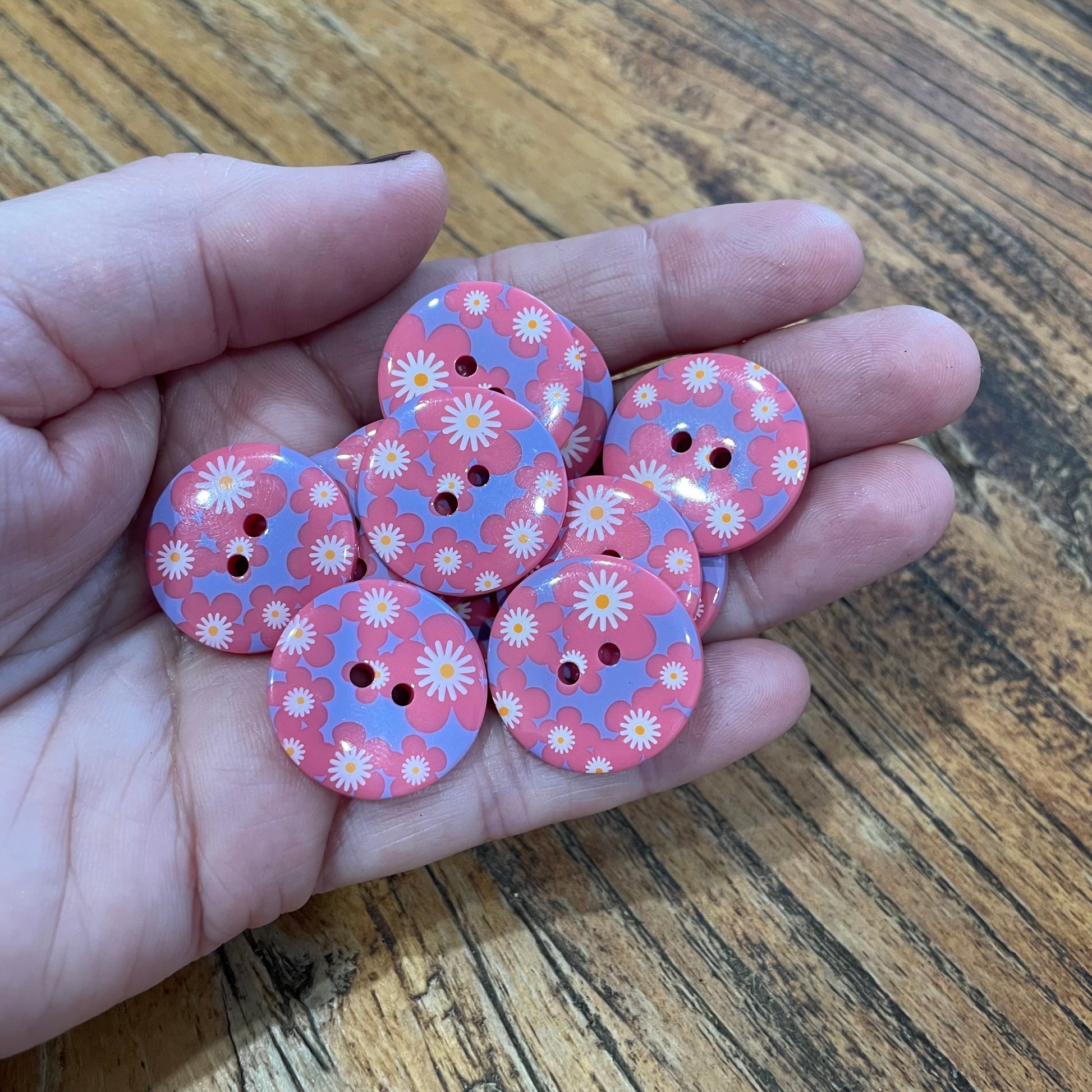 Hand holding pink floral buttons on a wooden surface