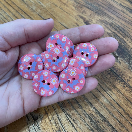 Hand holding pink floral buttons on a wooden surface