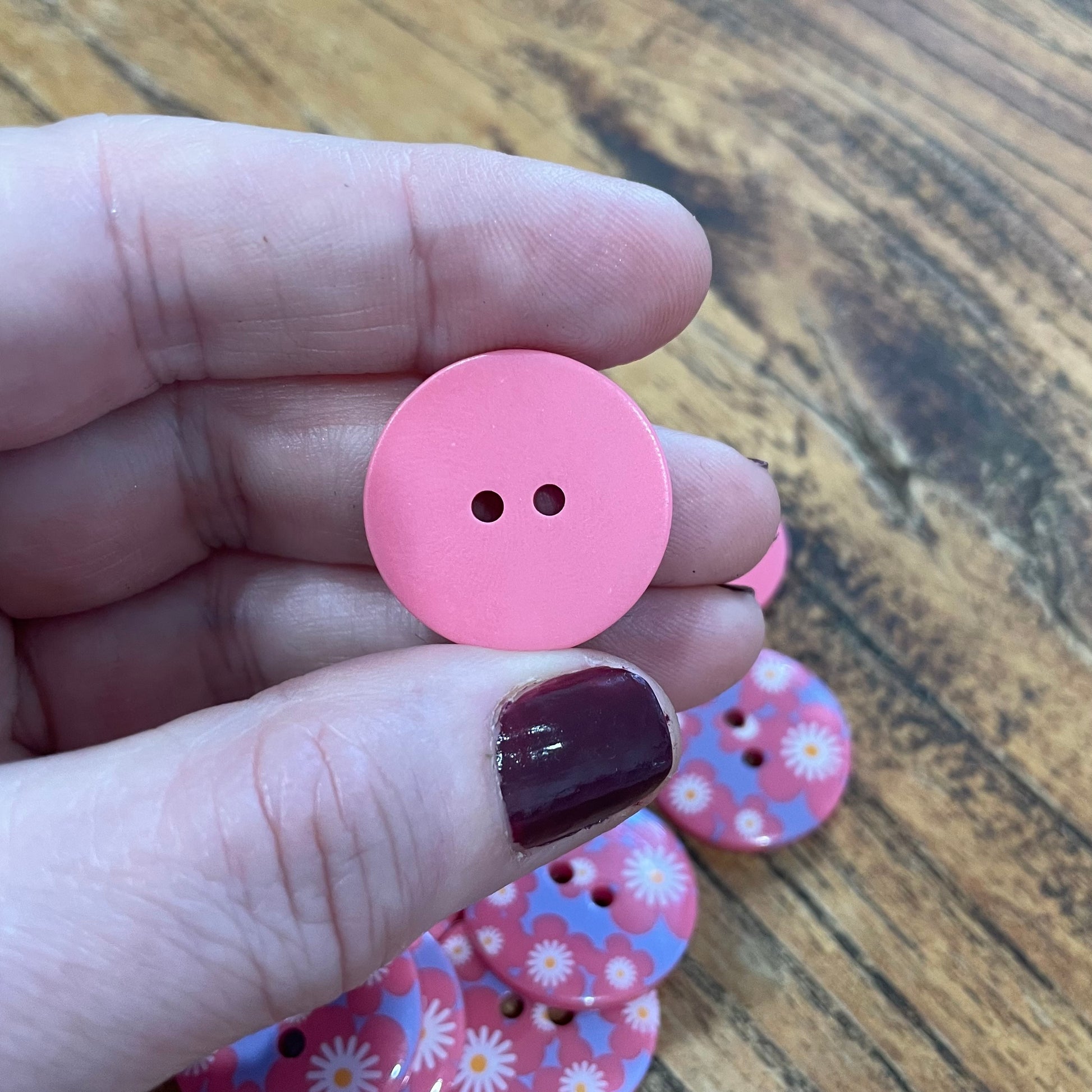 Pink button held between fingers with more buttons on a wooden surface