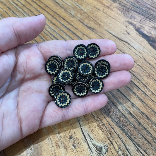 Hand holding a small collection of decorative buttons with intricate designs on a wooden surface.