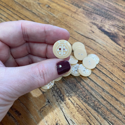 Hand holding a small beige button with a wooden surface in the background