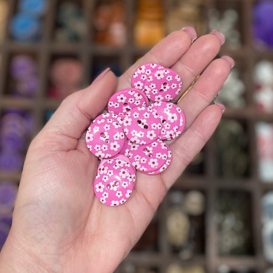 A hand holding several pink flower-shaped resin buttons with two holes each, displayed in a craft setting.