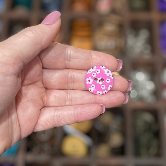 A hand holding several pink flower-shaped resin buttons with two holes each, displayed in a craft setting.