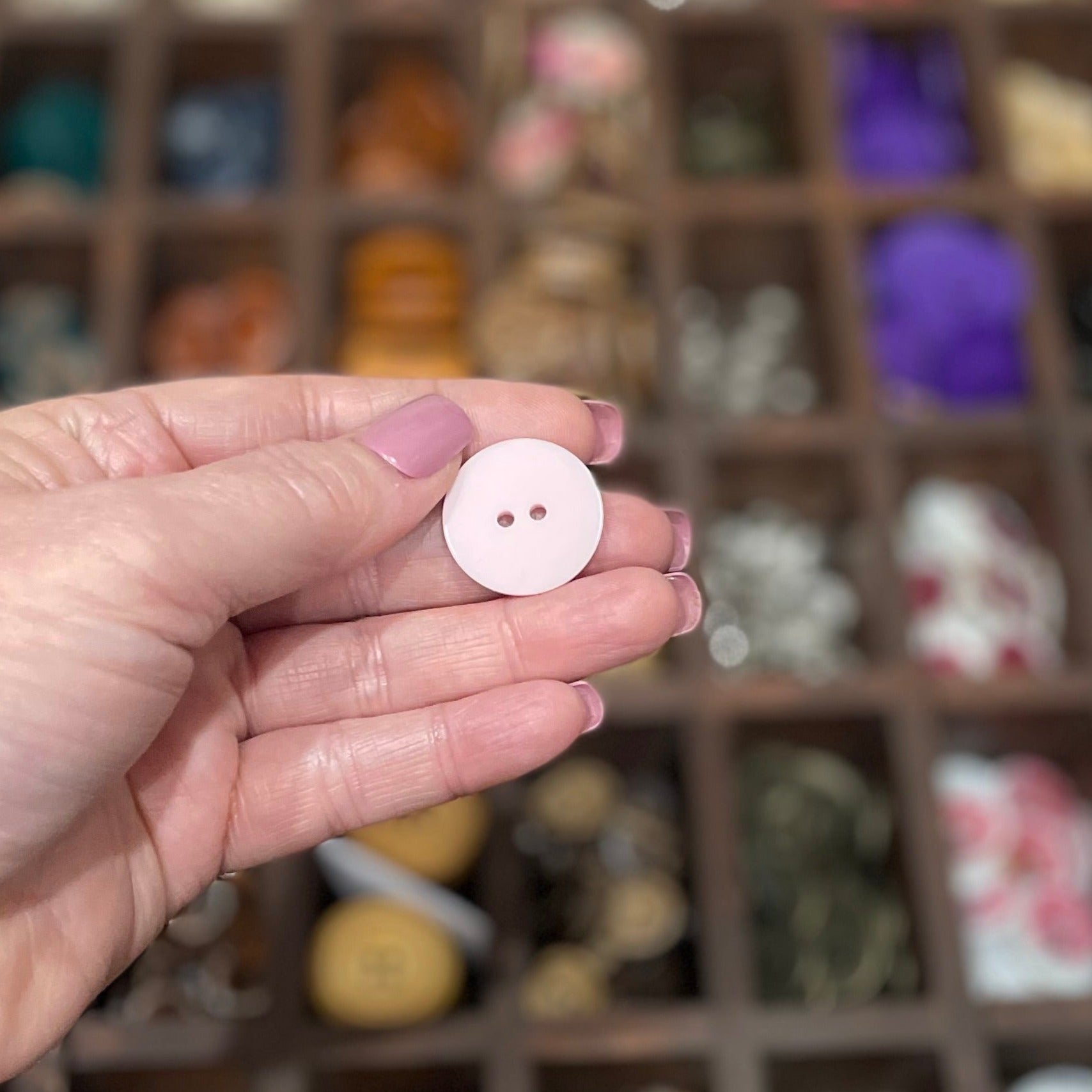 A hand holding a few pale pink resin buttons with a heart pattern and two holes each.