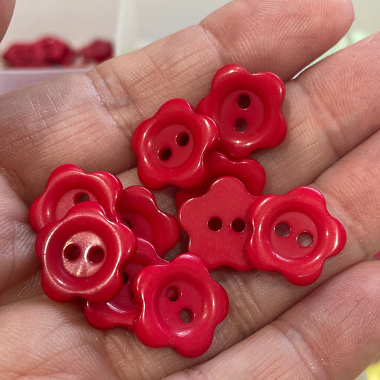 Hand holding red flower-shaped buttons with a blurred background of more buttons.