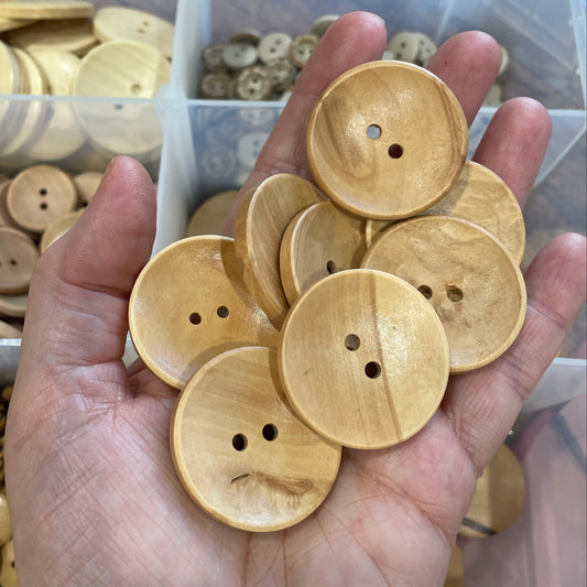 Hand holding wooden buttons with a clear container of buttons in the background