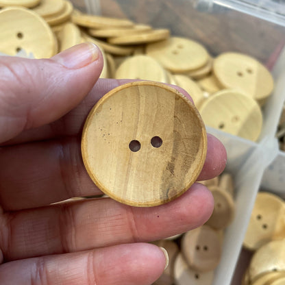Hand holding a wooden button with a container of buttons in the background