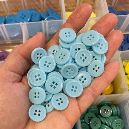 Hand holding light blue buttons with a container of buttons in the background