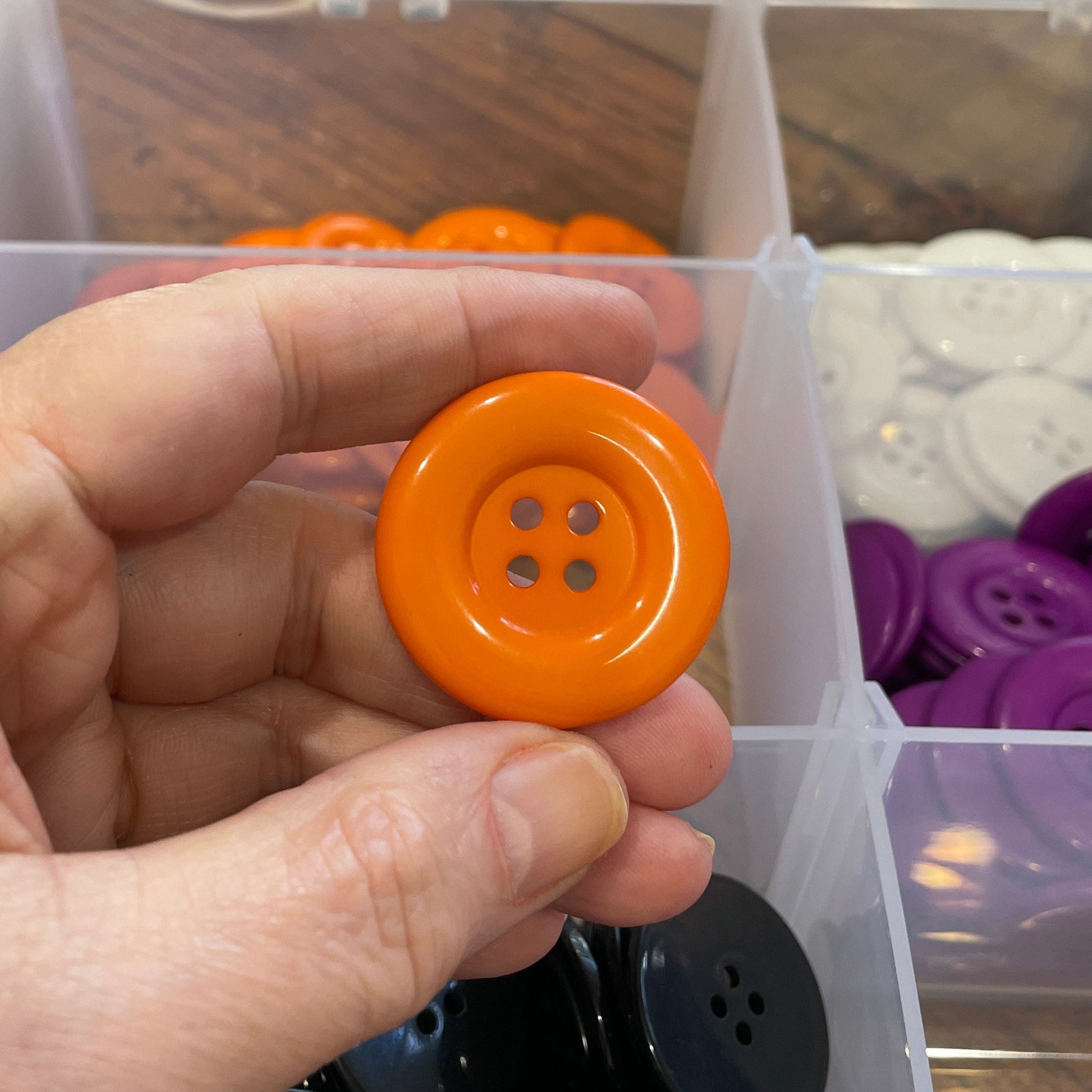 Hand holding an orange button with a clear container of buttons in the background