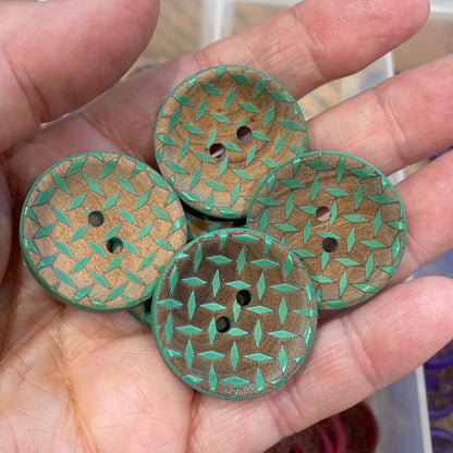 Hand holding three green textured buttons with a container of buttons in the background.