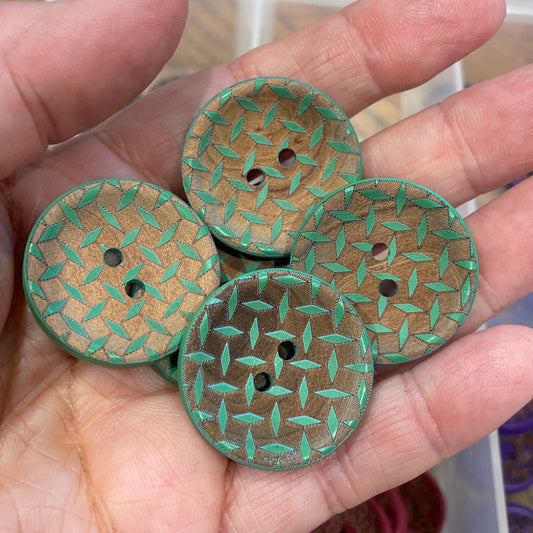 Hand holding three green textured buttons with a container of buttons in the background.