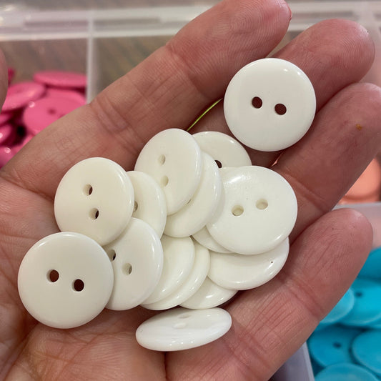 Hand holding white buttons with a background of colorful buttons in containers.