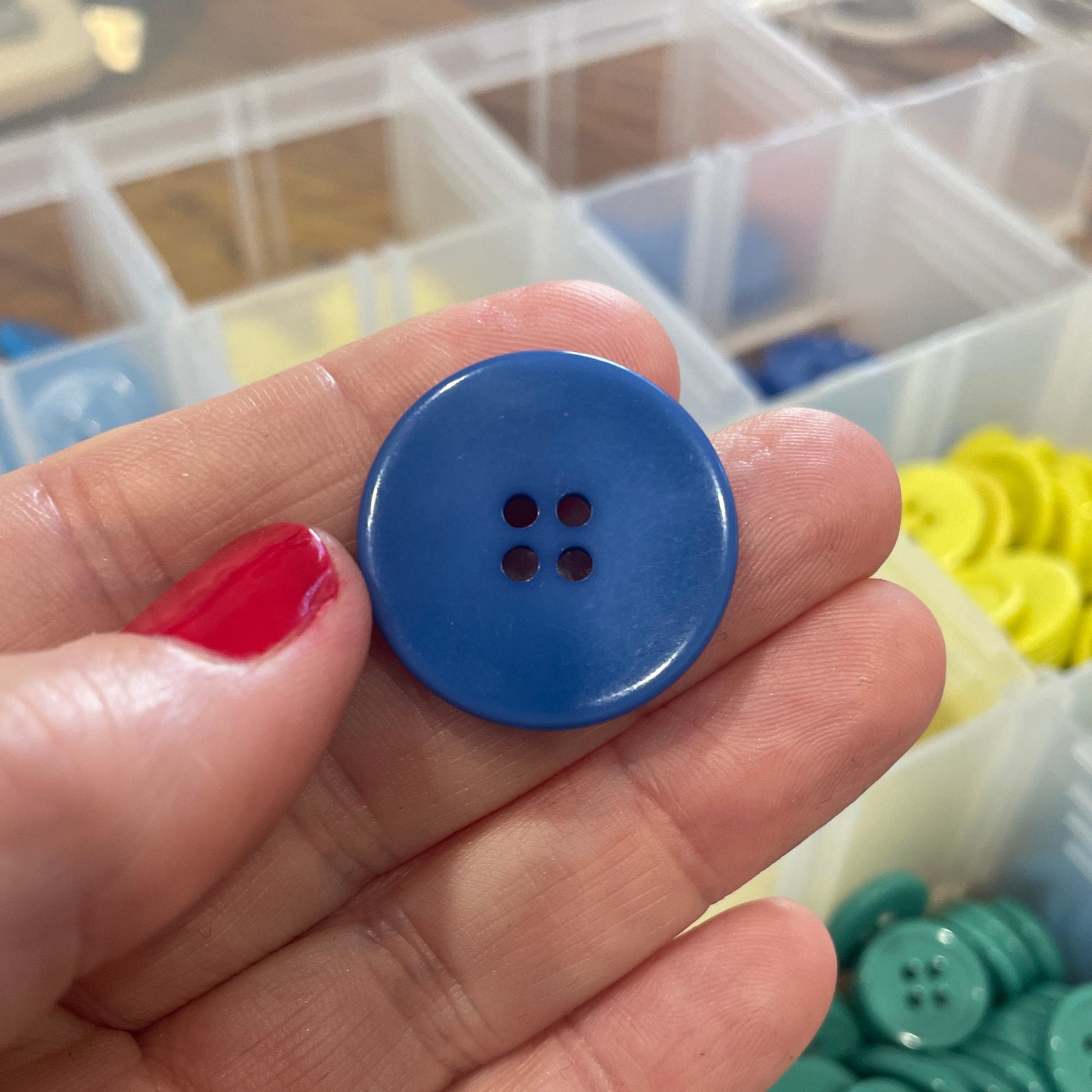 Blue button held in a hand with a container of buttons in the background