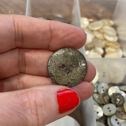 Hand holding a button with a background of various buttons in a container