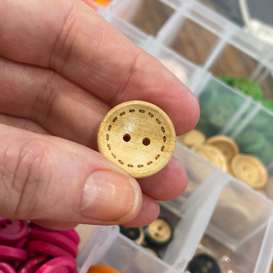 Hand holding a yellow button with a container of assorted buttons in the background.