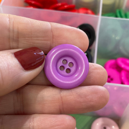 Hand holding a purple button with a container of assorted buttons in the background