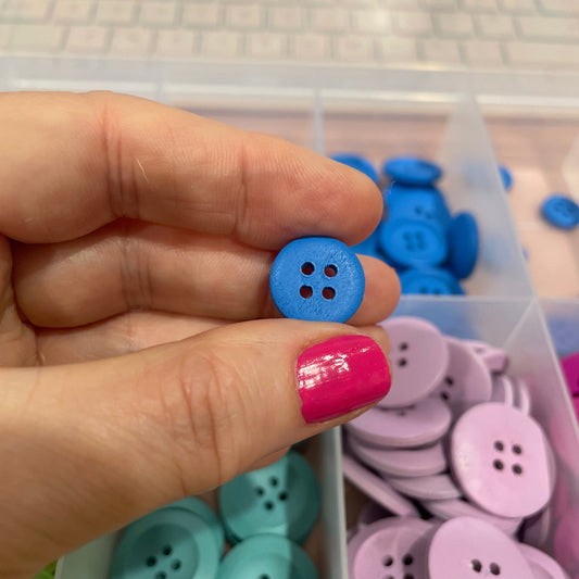 Hand holding a blue button with a container of buttons in the background