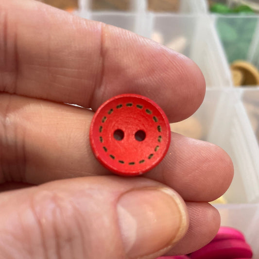 Red button held between fingers with a container of colorful buttons in the background