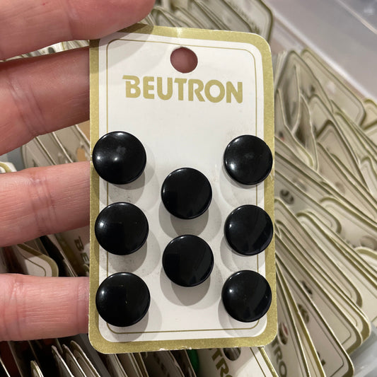 Hand holding a package of black buttons with 'Beutron' branding.