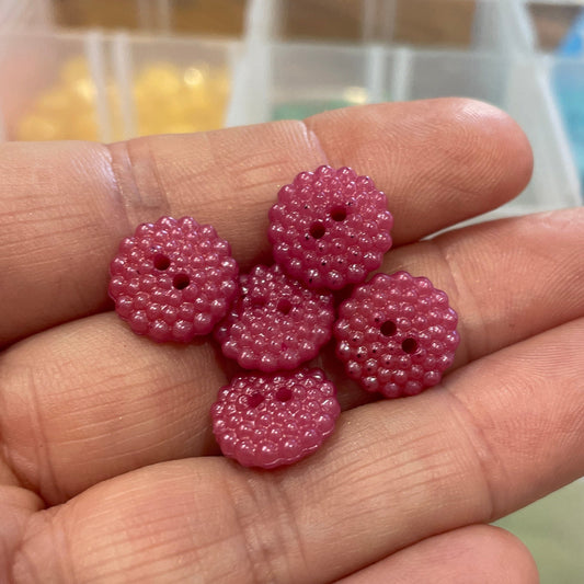Hand holding pink beads with a blurred background of storage containers.