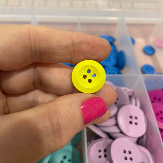 Hand holding a yellow button with a container of colorful buttons in the background
