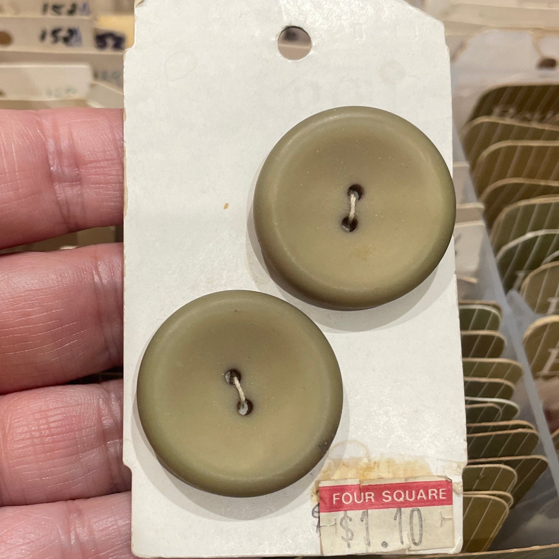 Two brown buttons on a white card held in a hand with a blurred background