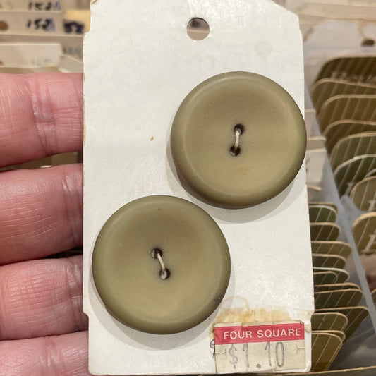 Two brown buttons on a white card held in a hand with a blurred background