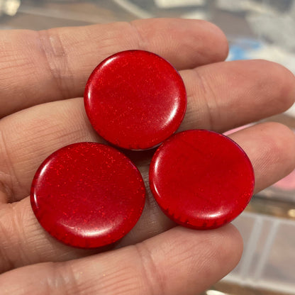 Three red buttons held in a hand with a blurred background of a storage box with more buttons.