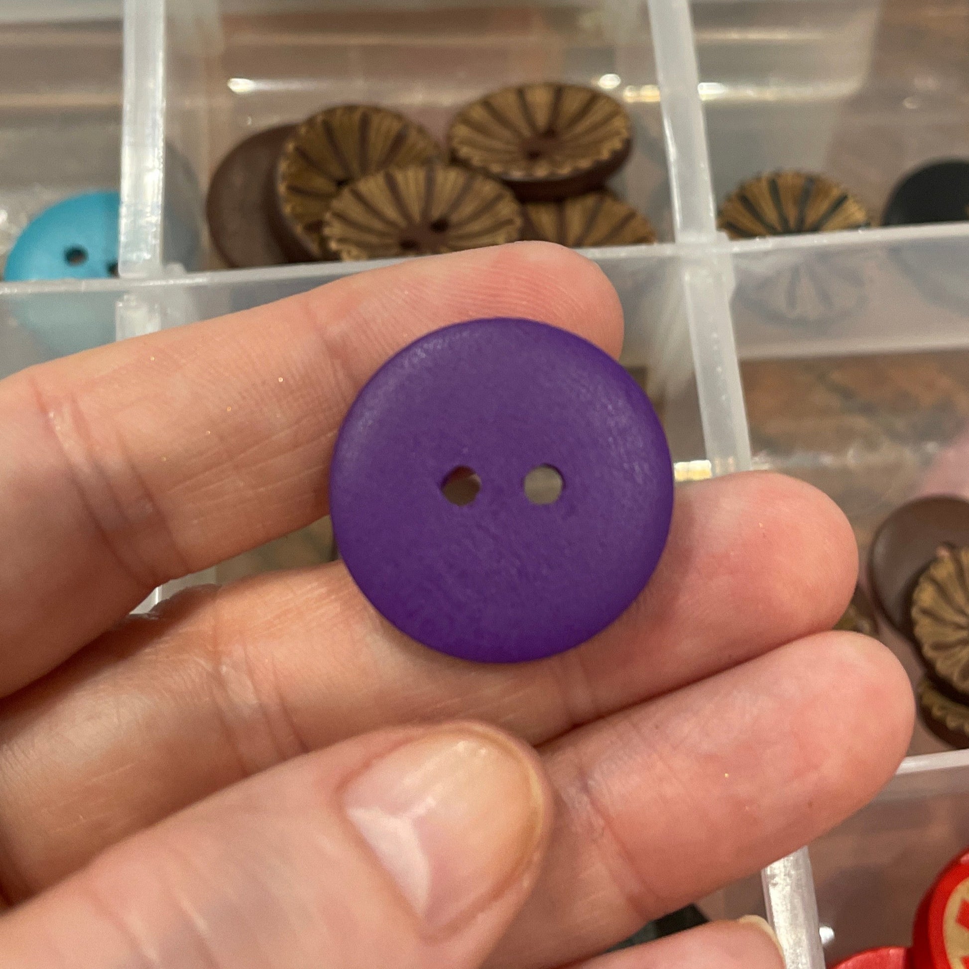 Purple button held by a hand with a container of various buttons in the background